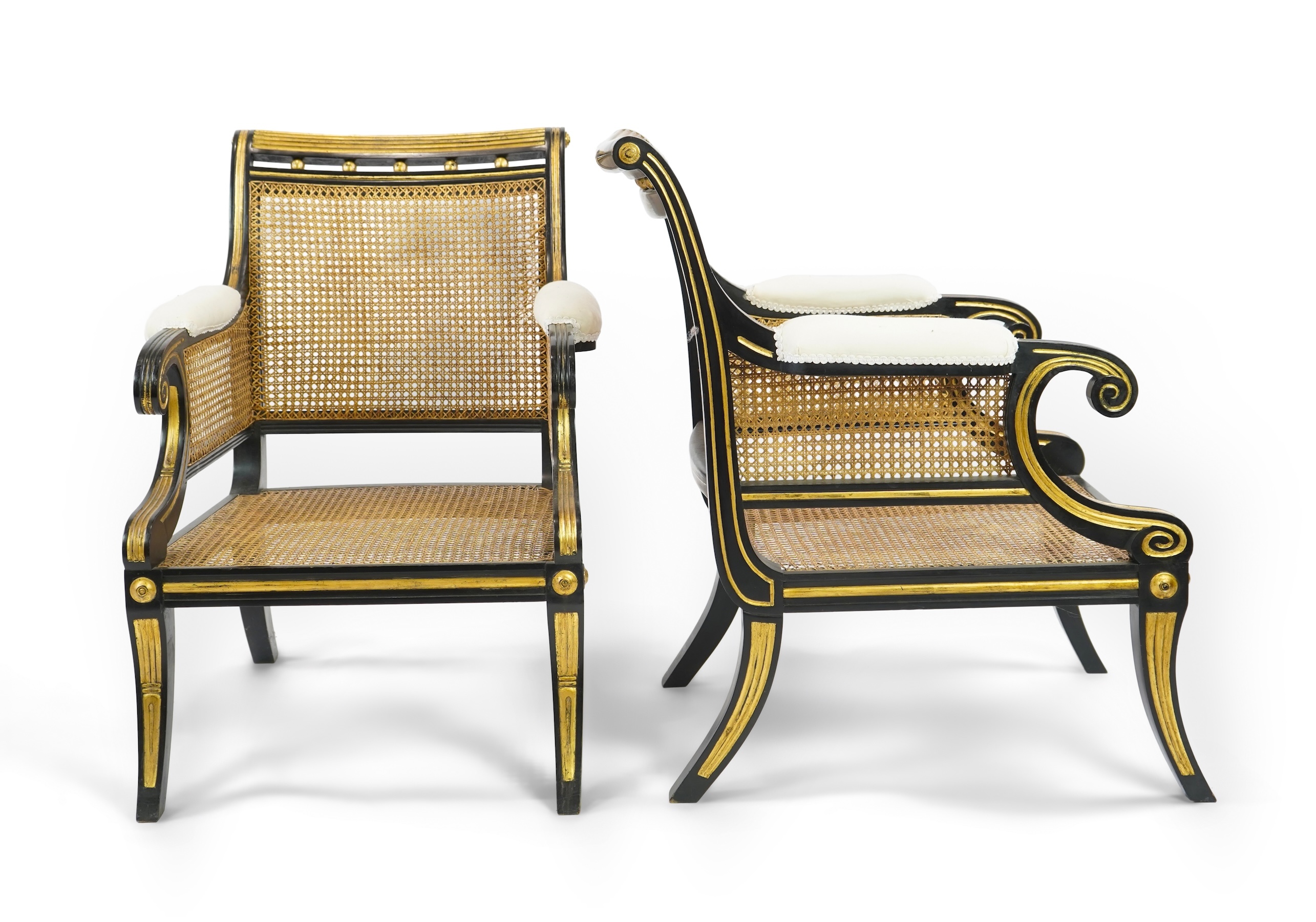 A pair of Regency style ebonised, parcel gilt caned bergere elbow chairs